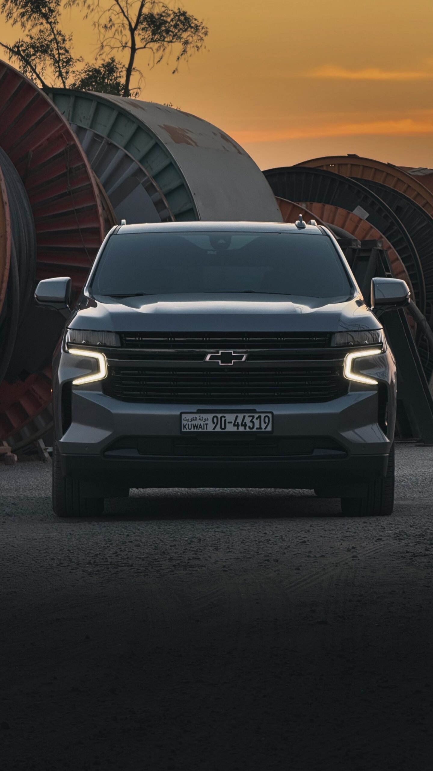 A sleek SUV photographed front-facing at sunset, set against industrial spools outdoors.