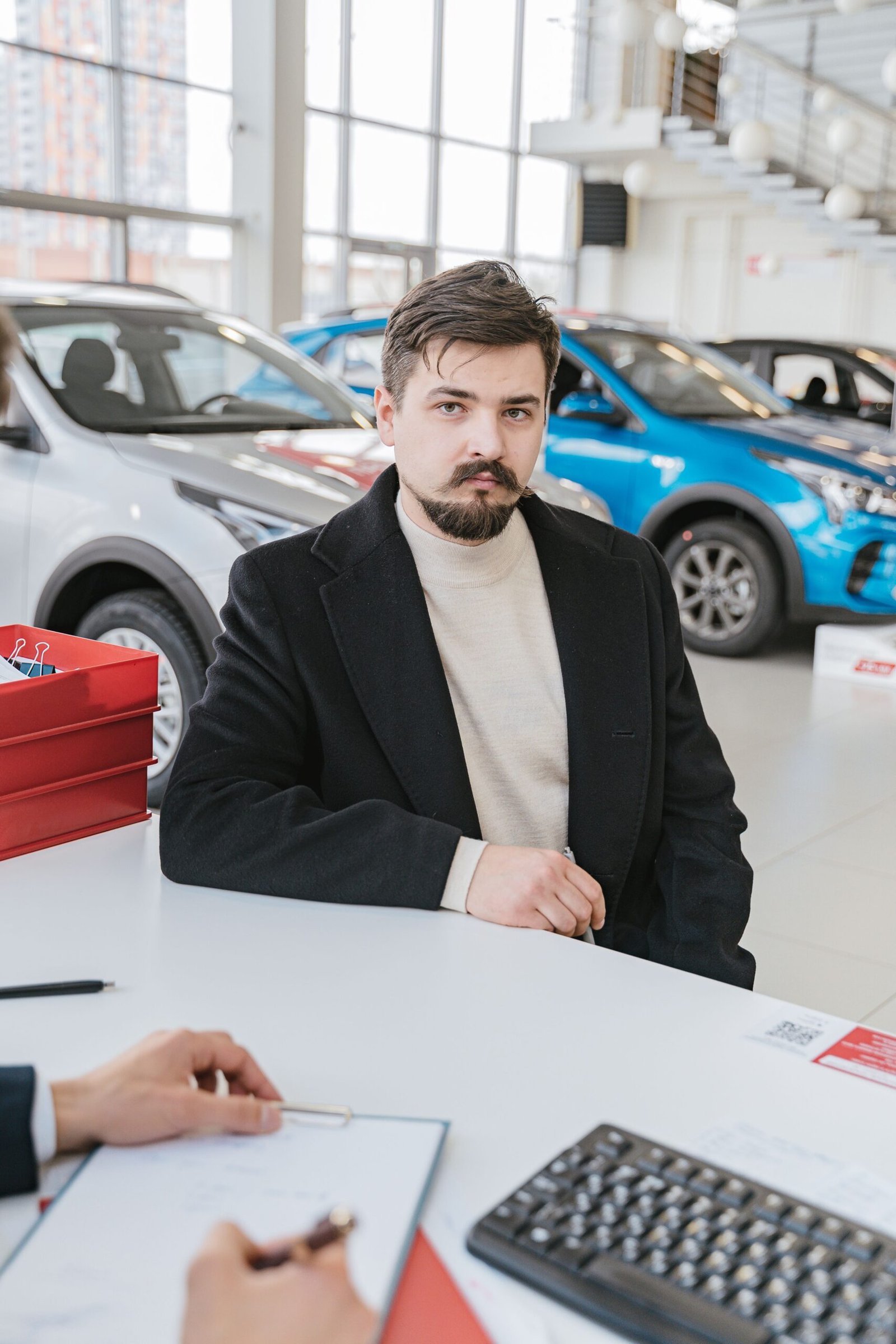 A man in a coat discusses with a sales representative in a bright, modern car showroom.